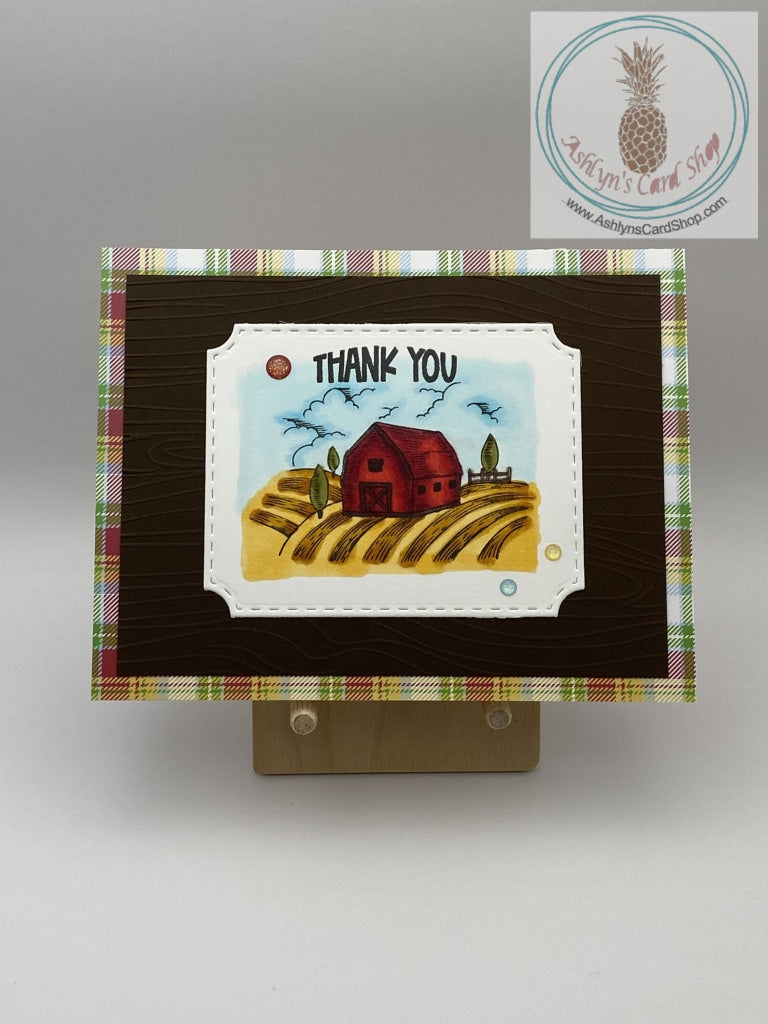 A thank you card with a farm theme. Hand coloured barn scene on brown cardstock and an additional layer of patterned paper (plaid shown). A2 size card 4.25 x 5.5". Coordinating envelope included.