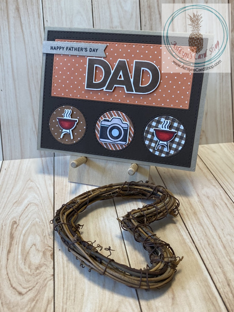 Father's Day card with a barbeque theme. High quality handmade greeting card with hand coloured images that represent Dads. Mounted to a kraft coloured card base, a dark brown die cut frame with inlaid pieces of patterned paper showcases the sentiments and coloured images in this design. Patterned paper varies amongst the versions. A2 Card Size: 4.25 x 5.5". Coordinating envelope included. Grill & Camera version.