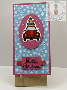 Car & Presents Christmas Card - A hand coloured Beetle-like car with wrapped Christmas presents piled on top. Available with a choice of two snowy backgrounds in either pink or red. External sentiment reads “All hearts come home for Christmas” and the internal sentiment reads “Be Merry”. Mini slim size: 3.25 x 6.25”. Coordinating envelope included.
