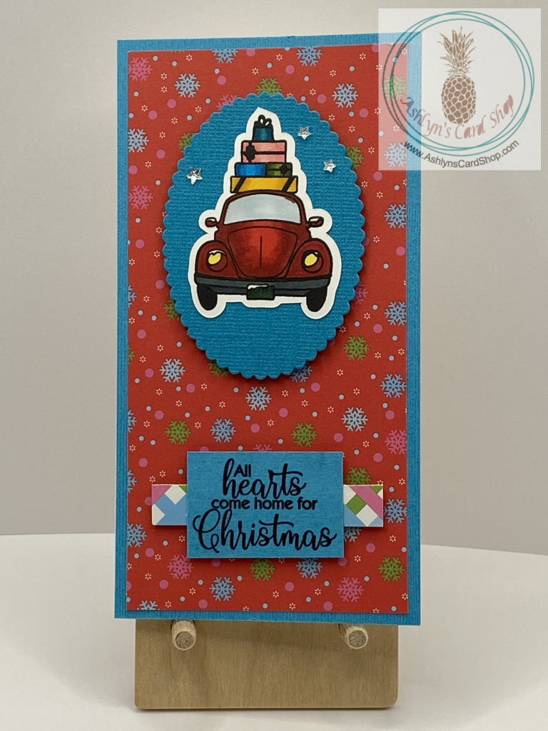 Car & Presents Christmas Card - A hand coloured Beetle-like car with wrapped Christmas presents piled on top. Available with a choice of two snowy backgrounds in either pink or red (shown). External sentiment reads “All hearts come home for Christmas” and the internal sentiment reads “Be Merry”. Mini slim size: 3.25 x 6.25”. Coordinating envelope included.