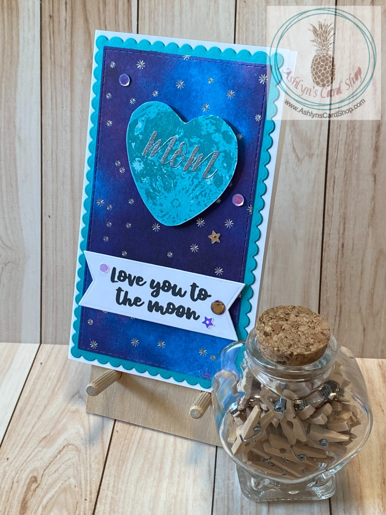 Galaxy themed Mother's Day card with a heart shaped moon popped up on a starry patterned paper background adorned with coordinating sequins. "Mom" is heat embossed on the moon. External sentiment reads "love you to the moon" and the internal sentiment adds a little humour: "thanks for the genes . . . no wonder I'm awesome!" Teal version shown. Mini slim card size 3.5 x 6". Coordinating envelope included.