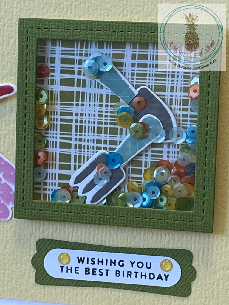 Close up of the shaker box on the front of the Gardener's Birthday Card (Shaker) available at Ashlyn's Card Shop. Shaker includes gardening tools die cuts and multiple colours of sequins.