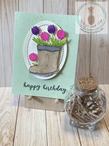 Watercoloured gardening boots filled with pink and purple tulips are popped up on a decorative cream coloured oval. The oval is popped up on a colourful speckled patterned paper background.  The sentiment on the front reads "happy birthday"; the internal sentiment reads "you are SO worth celebrating". Green version shown. A2 card size: 4.25 x 5.5". Coordinating envelope included.