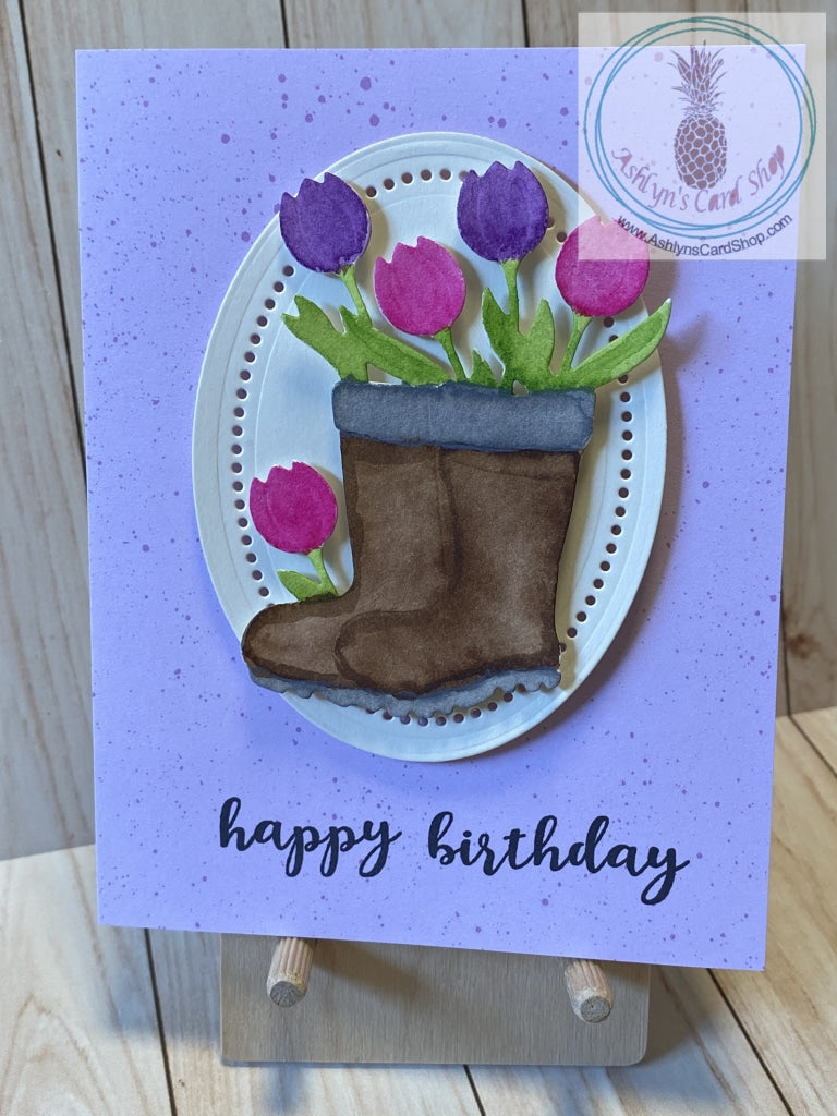 Watercoloured gardening boots filled with pink and purple tulips are popped up on a decorative cream coloured oval. The oval is popped up on a colourful speckled patterned paper background.  The sentiment on the front reads "happy birthday"; the internal sentiment reads "you are SO worth celebrating". Purple version shown. A2 card size: 4.25 x 5.5". Coordinating envelope included.