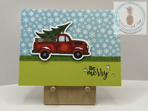 Getting The Christmas Tree Card - A hand coloured image of a truck bringing home a fresh Christmas tree. Available  in two snowy background options: pink and blue (shown). External sentiment reads “Be merry” and the internal sentiment reads “Happy Holidays”.  A2 size card: 4.25 x 5.5”. Coordinating envelope included.
