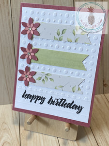 High quality handmade greeting card featuring layered pink flowers and banners of coordinating patterned paper on white card panel embossed with dots and stamped with "happy birthday". The white panel is attached to a pink cardstock background on a white card base.  Internal sentiment reads "make a wish". Green version. A2 card size: 4.25 x 5.5".  Coordinating envelope included.