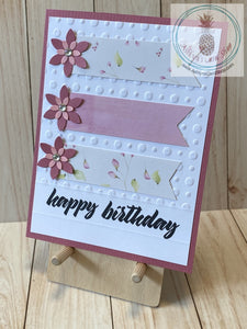 High quality handmade greeting card featuring layered pink flowers and banners of coordinating patterned paper on white card panel embossed with dots and stamped with "happy birthday". The white panel is attached to a pink cardstock background on a white card base.  Internal sentiment reads "make a wish". Pink version. A2 card size: 4.25 x 5.5".  Coordinating envelope included.