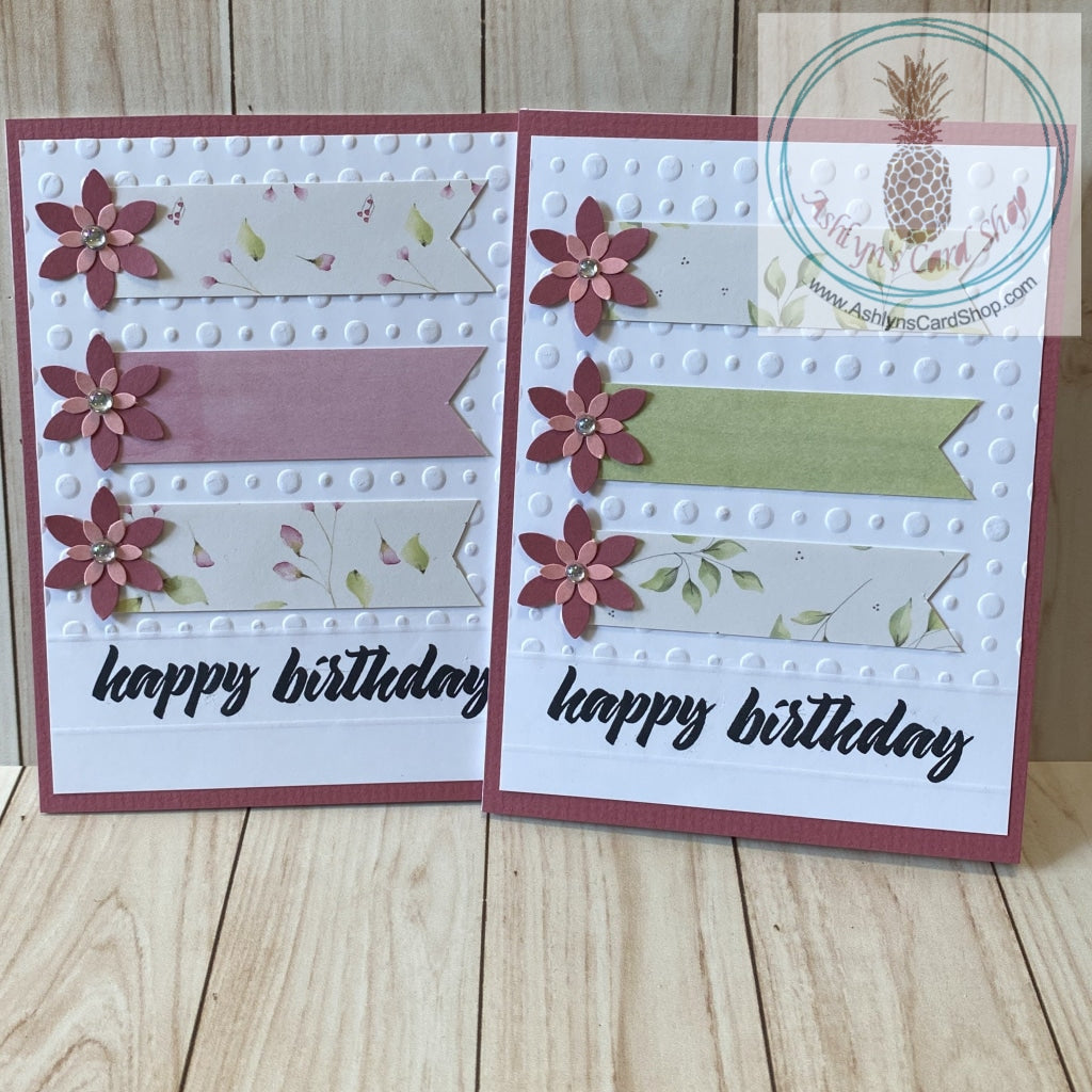 High quality handmade greeting card featuring layered pink flowers and banners of coordinating patterned paper on white card panel embossed with dots and stamped with "happy birthday". The white panel is attached to a pink cardstock background on a white card base.  Internal sentiment reads "make a wish". Pink and green versions shown. A2 card size: 4.25 x 5.5".  Coordinating envelope included.