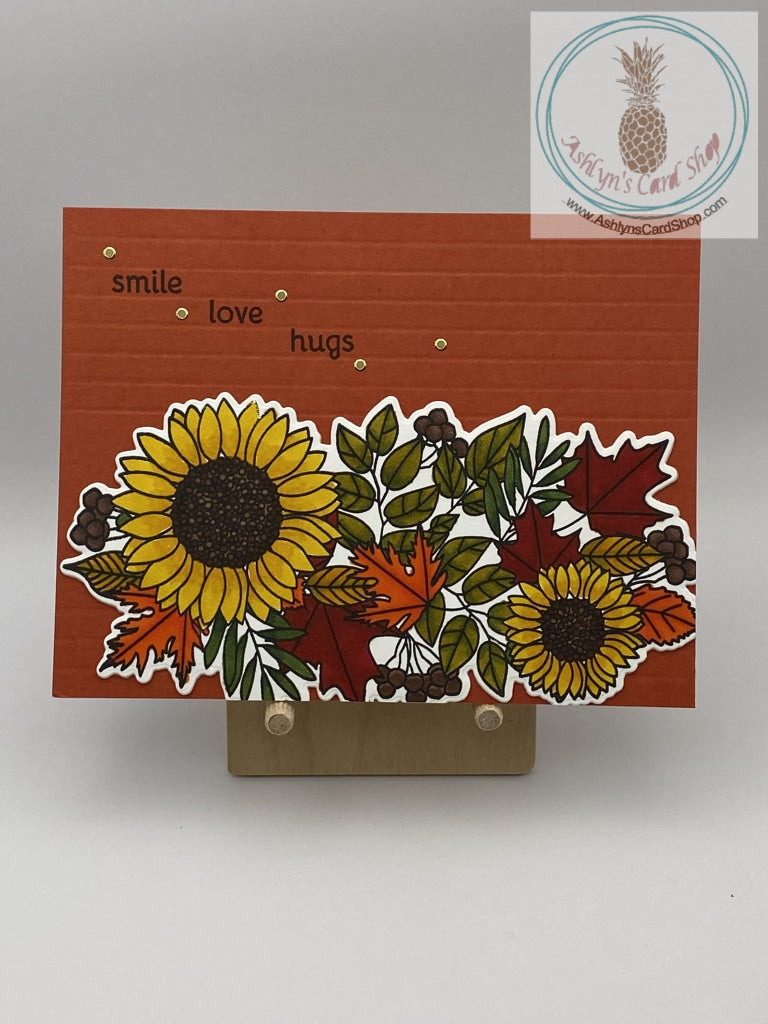 Hand coloured fall floral collage on an embossed orange background. External sentiment reads: smile love hugs; inside of card is blank for your personal message. A2 size card 4.25 x 5.5". Coordinating envelope included.