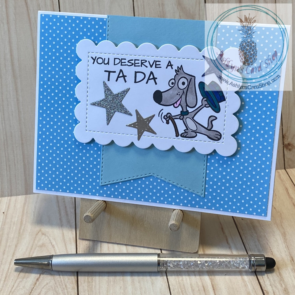 A cute magical puppy says your dad deserves a Ta Da! Hand coloured cartoon dog with a hat and cane stamped on a white scalloped rectangle that is popped up over a large banner (with stitched detail) in a colour that coordinates with the polka dot patterned paper background. External sentiment reads "you deserve a TA DA"; internal sentiment reads "Dad, thanks for everything that you do". A2 card size: 4.25 x 5.5". Coordinating envelope included. Light blue version.
