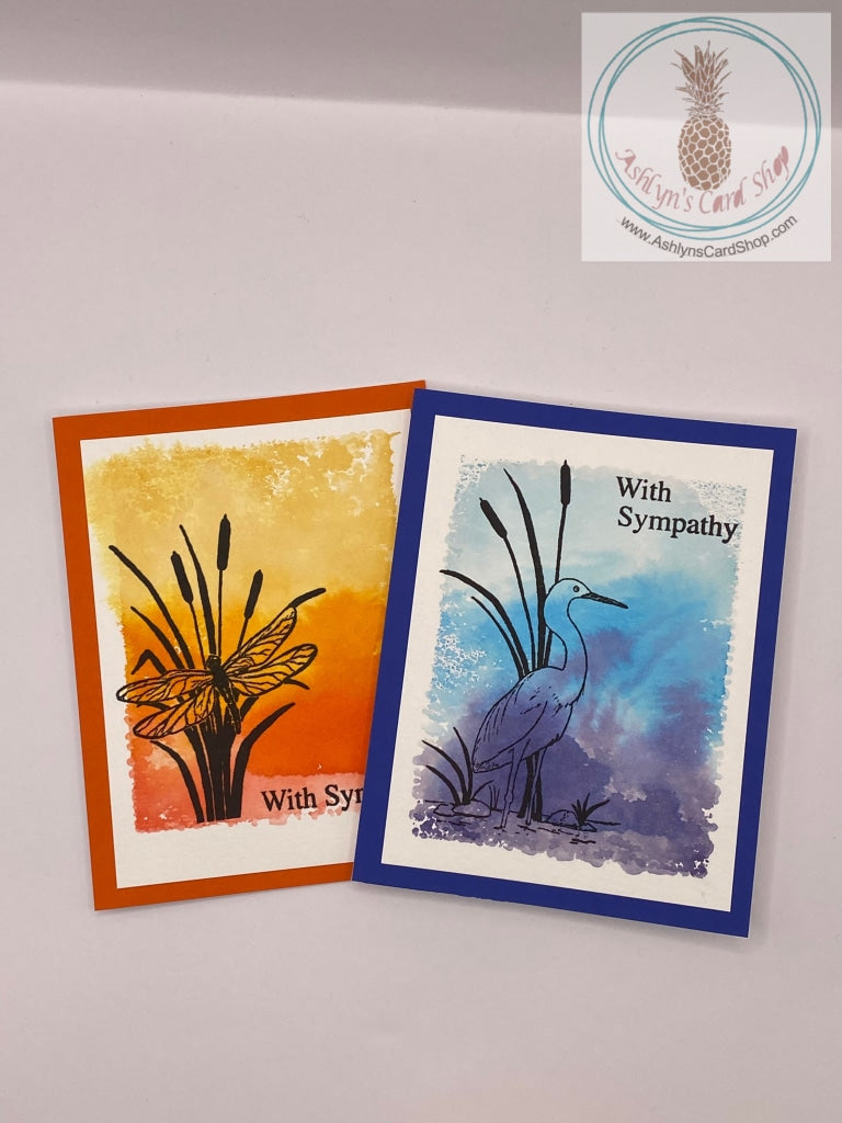 Sympathy card with a watercolour wash background stamped with either a dragonfly (on orange) or a crane (on blue) in silhouette. The dragonfly card sentiments read: with sympathy (external) and may your heart find comfort (internal). The crane card sentiments read: with sympathy (external) and thinking of you at this very sad time (internal).  A2 sized card: 4.25 x 5.5". Coordinating envelope included.